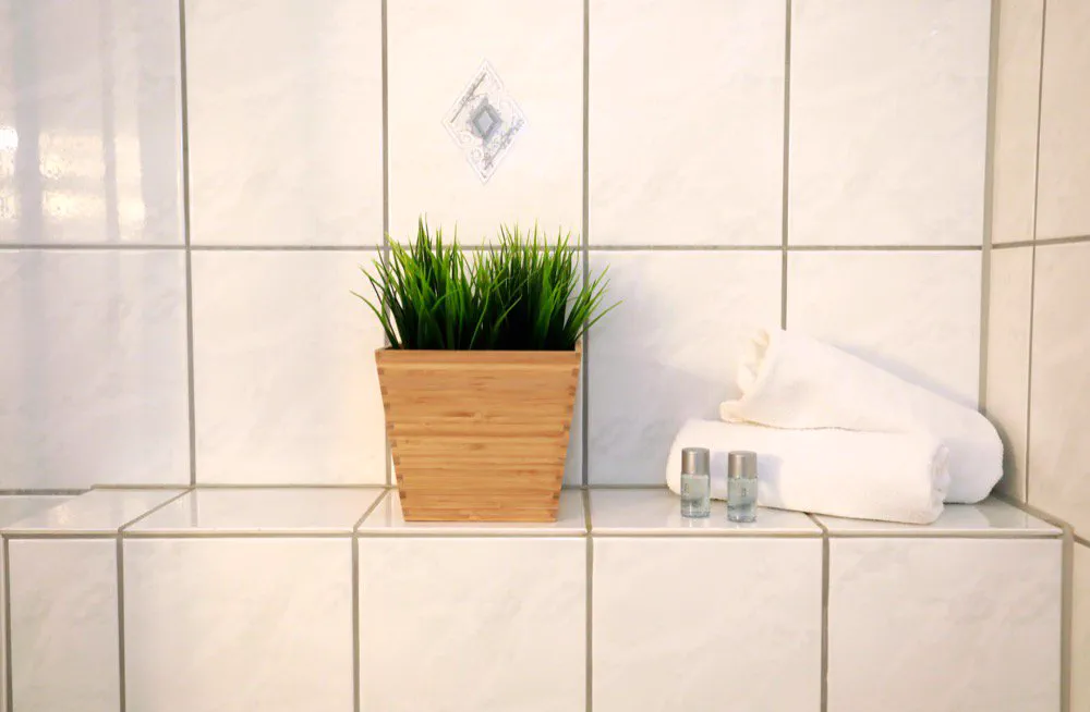 Badezimmer mit weißen Fliesen, frischen Handtüchern und Pflegeprodukten