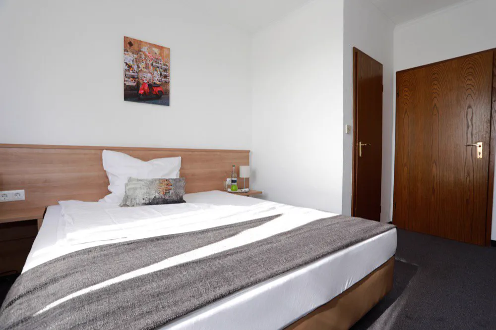 Doppelzimmer mit Kopfteil aus hellem Holz und weißer Bettwäsche