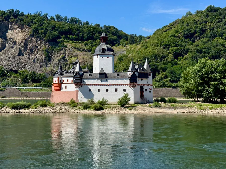 Weiße Burg auf einer Insel im Rhein vor bewaldeten Hängen